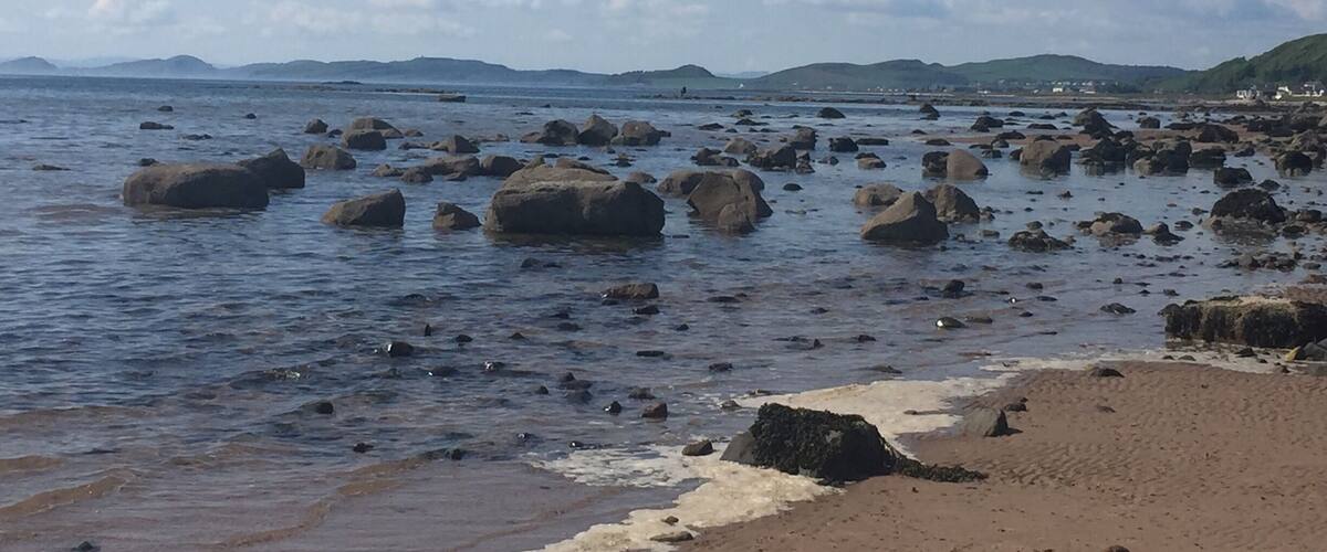 A rocky shoreline with waves gently lapping at the sand.