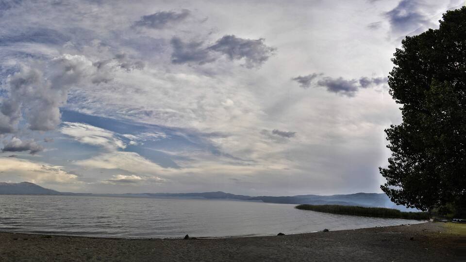 A lake with boats, a sandy beach, and mountains in the background.