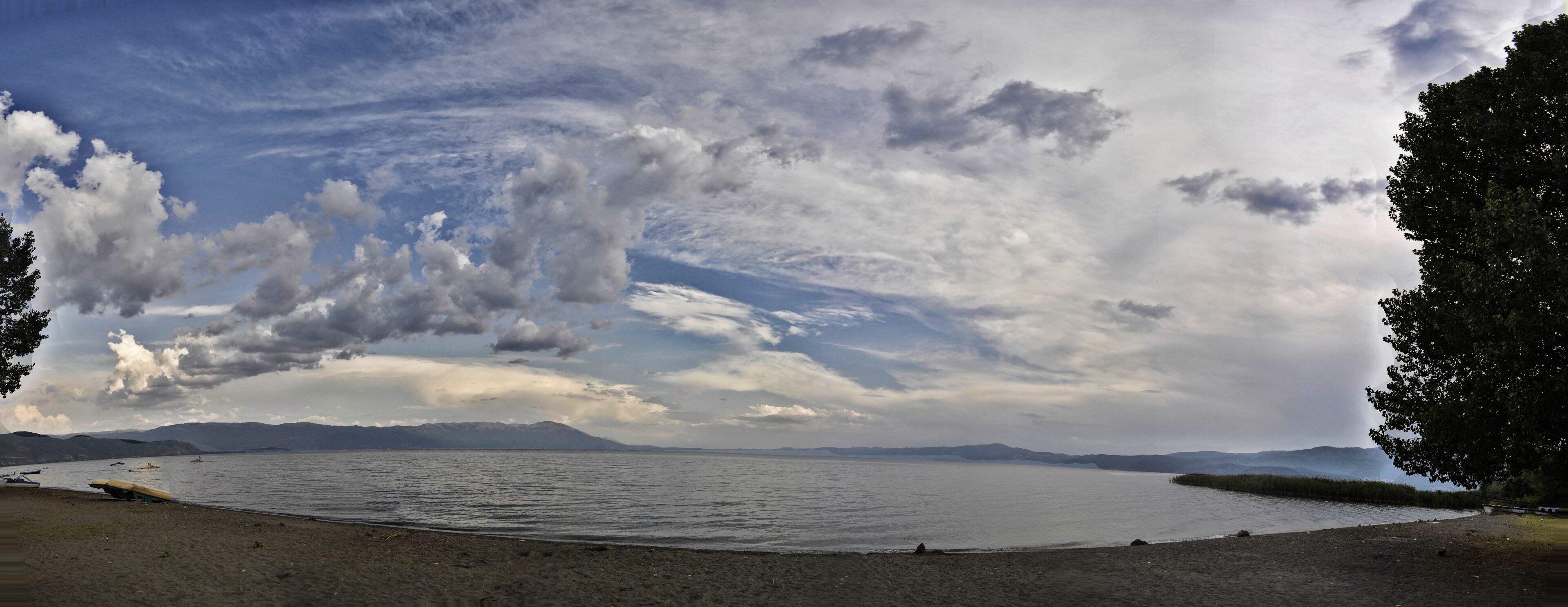 A lake with boats, a sandy beach, and mountains in the background.