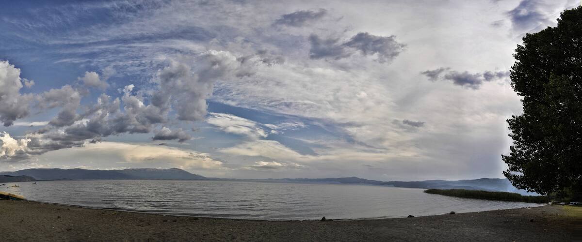 A lake with boats, a sandy beach, and mountains in the background.