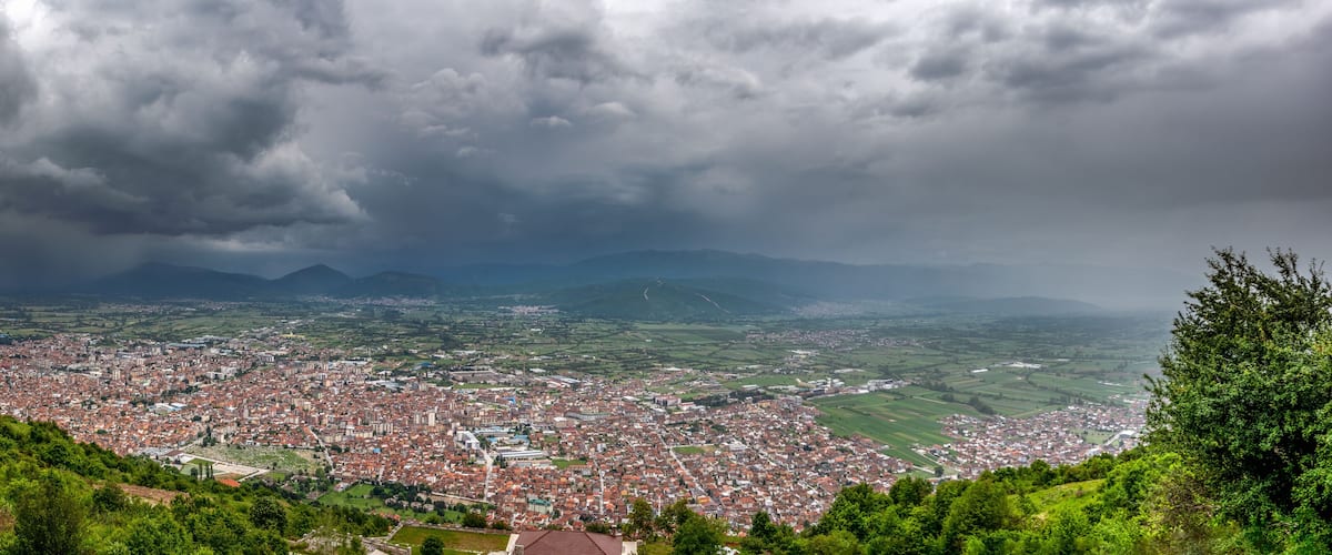 A cityscape with a mountainous backdrop under a cloudy sky.