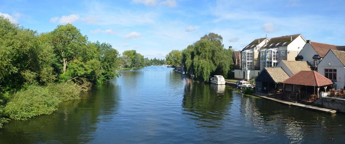 A river flanked by lush greenery and traditional buildings with red-tiled roofs.