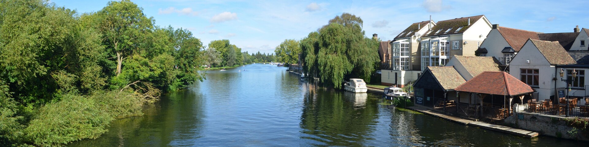 A river flanked by lush greenery and traditional buildings with red-tiled roofs.