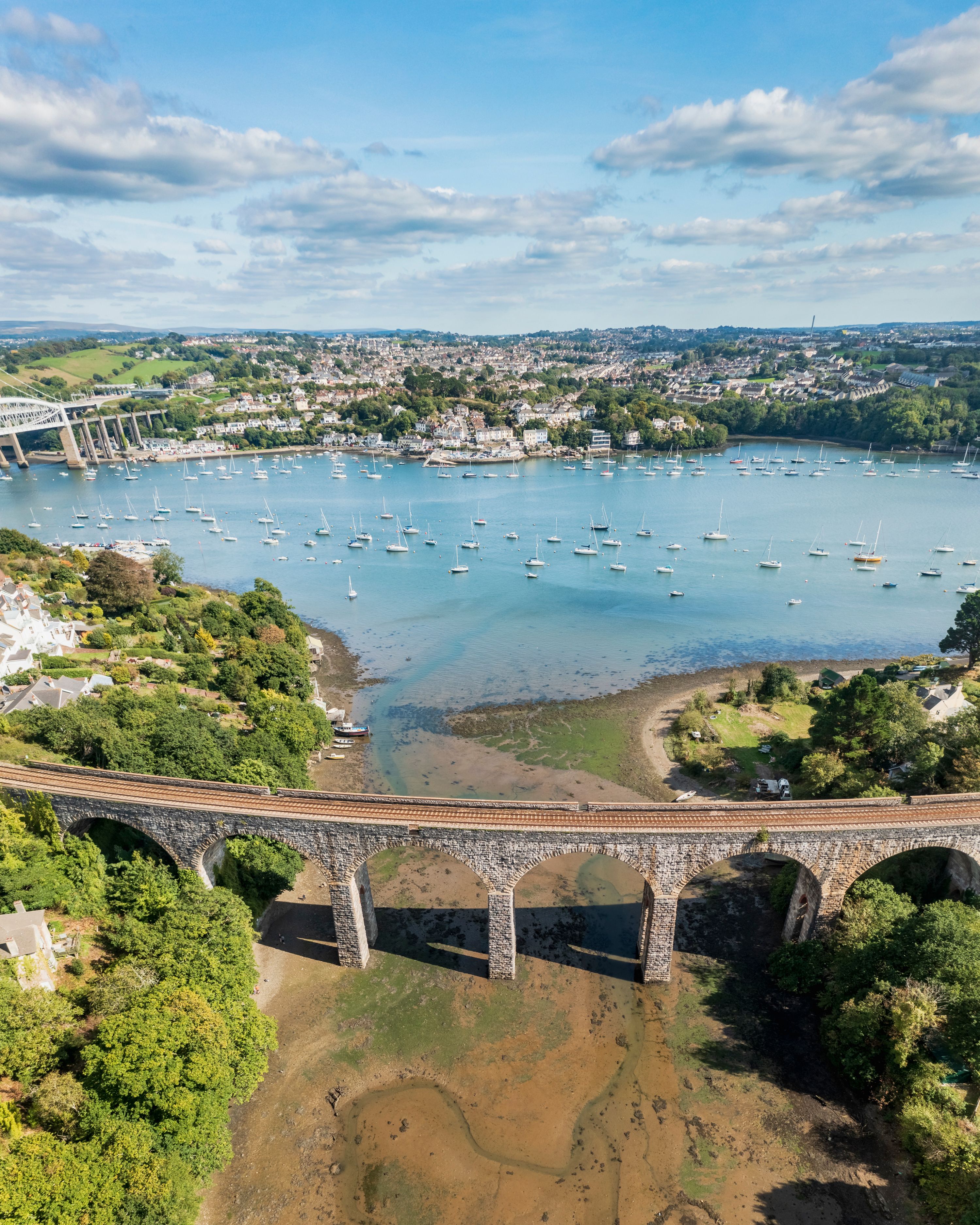 A coastal town with a bridge over a river, boats in the water, and greenery around.