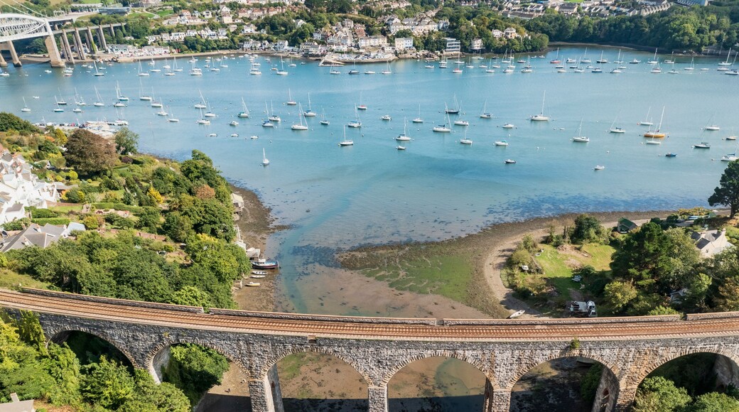 A coastal town with a bridge over a river, boats in the water, and greenery around.