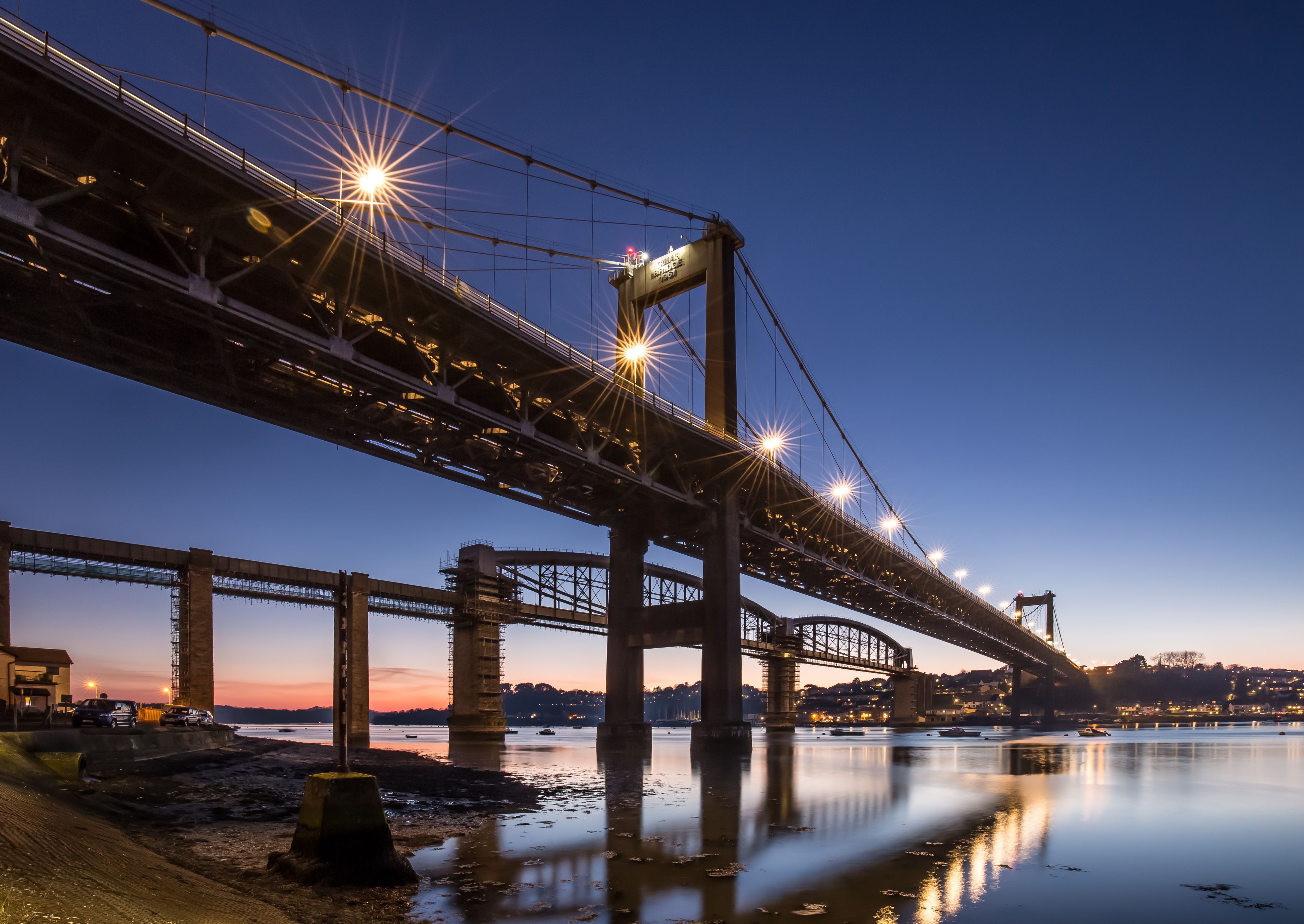 A large suspension bridge at dusk with lights reflecting on the water.