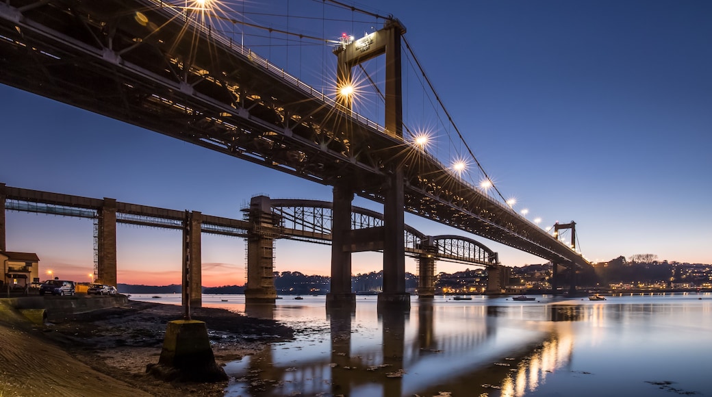 A large suspension bridge at dusk with lights reflecting on the water.