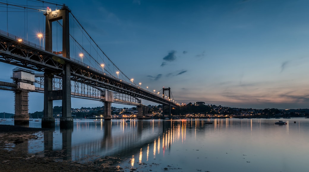 A large suspension bridge at dusk with lights reflecting on the water.