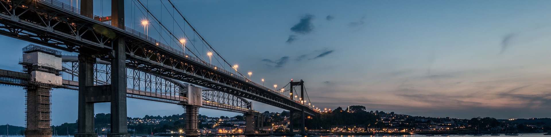 Un gran puente colgante al anochecer, con luces reflejadas en el agua.