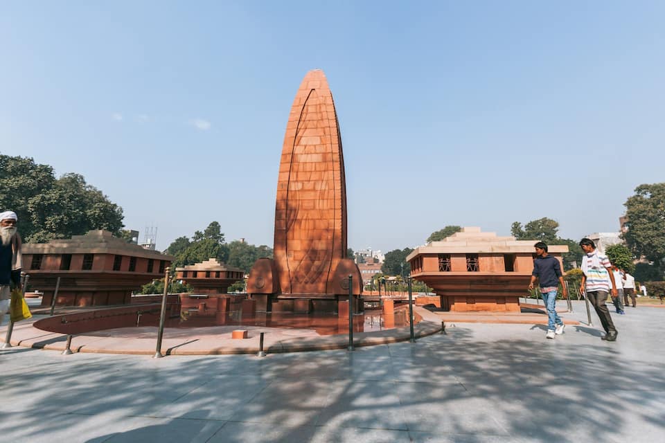 A tall, narrow obelisk monument surrounded by a plaza with people walking around.
