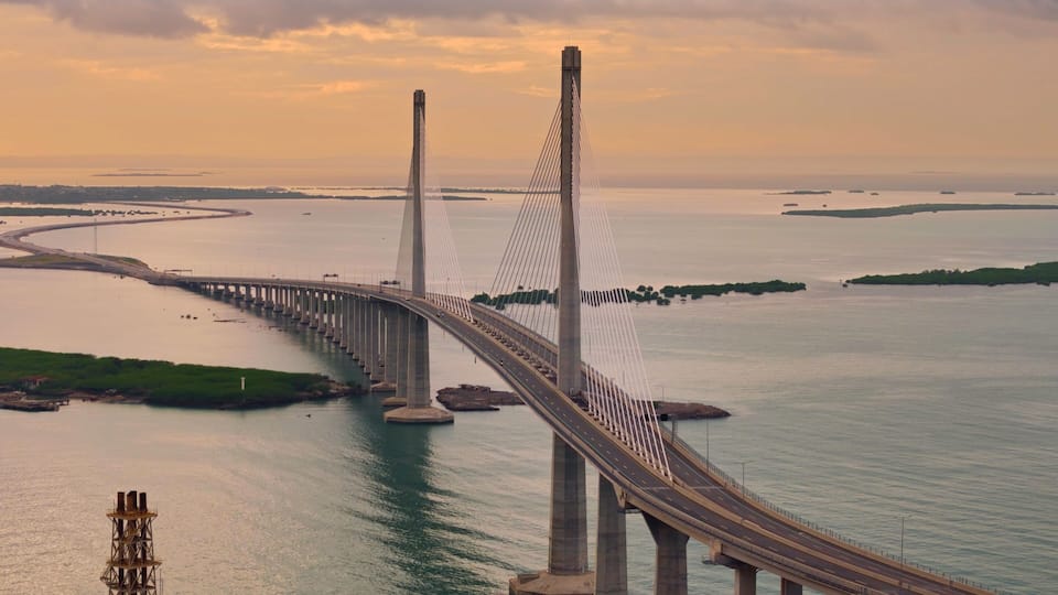 A cable-stayed bridge with a curved roadway, spanning over a body of water with islands in the distance.