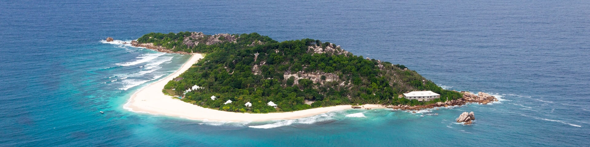 An island with a white sandy beach, lush green vegetation, and clear blue waters.