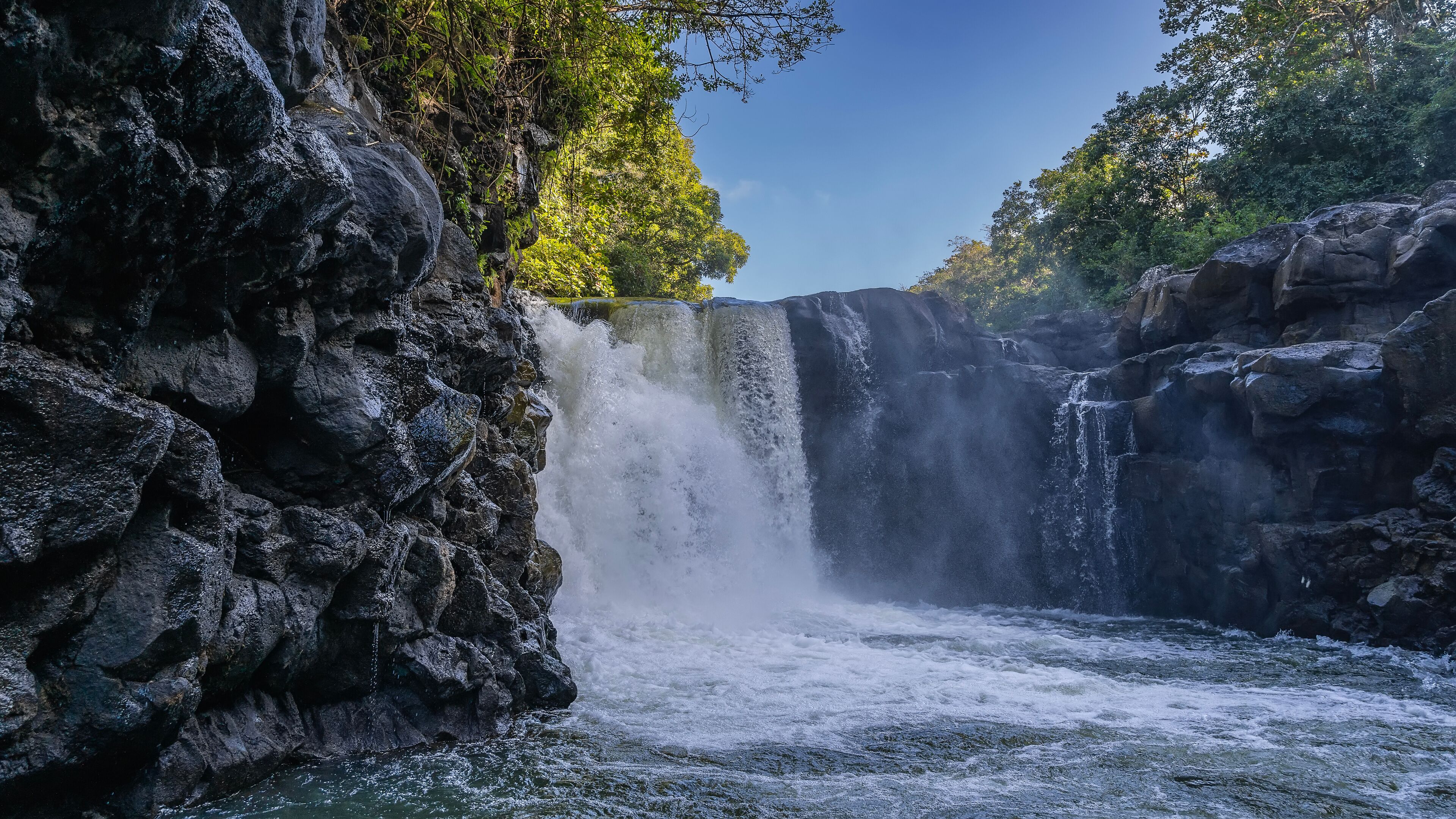 A waterfall cascading down a rocky cliff surrounded by lush greenery.