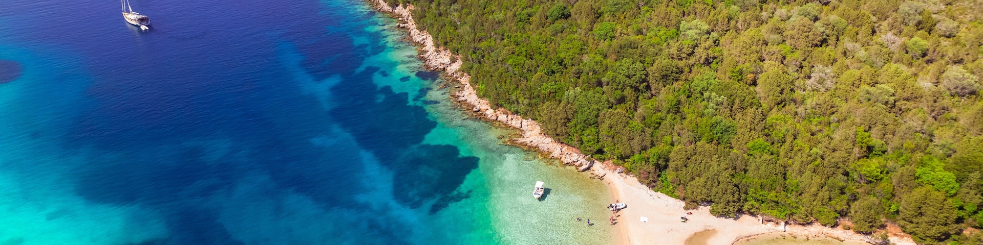 Paisagem costeira com águas turquesa cristalinas, uma praia arenosa e uma área arborizada.