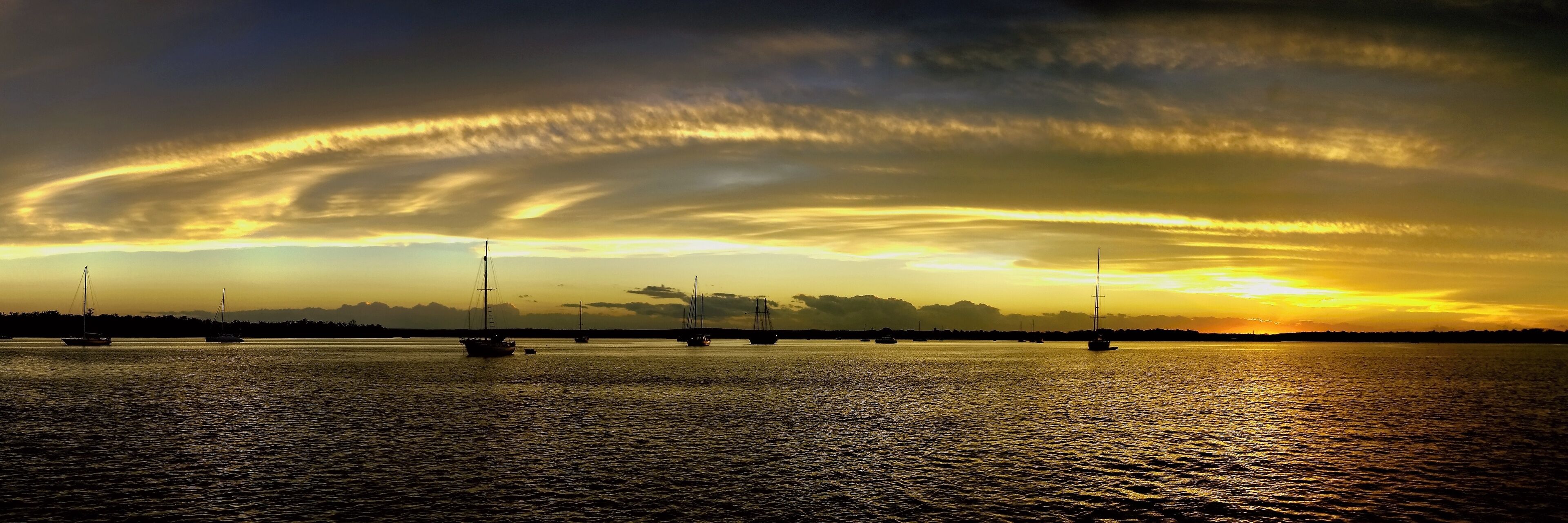A sunset over a calm sea with sailboats.