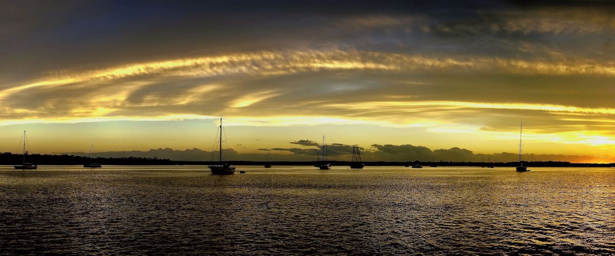 A sunset over a calm sea with sailboats.