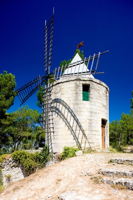 Een windmolen met een metalen spijnbekleding, een klein deurtje en een vlag aan de bovenkant, voor een strakblauwe hemel.