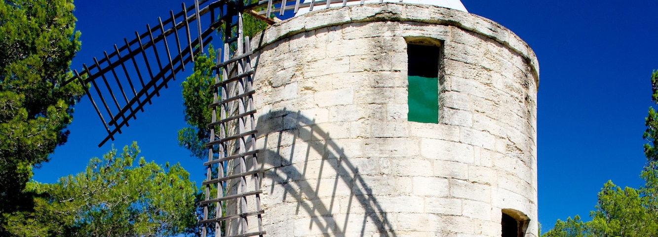 Un molino de viento con estructura metálica reticular, una puerta pequeña y una bandera en la parte superior, sobre un cielo azul despejado.