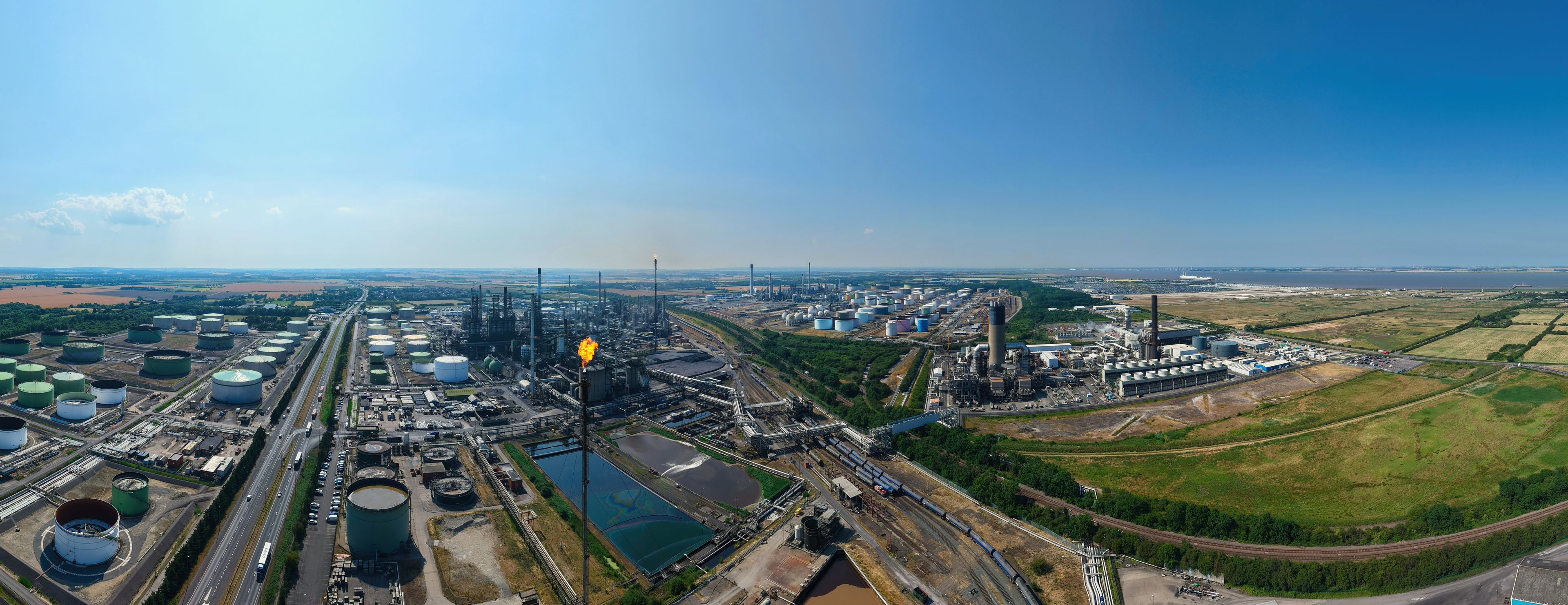 An industrial complex with multiple storage tanks, a railway line, and a large body of water.