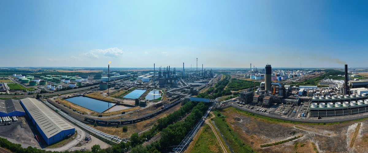 Aerial view of the Humber Refinery industrial complex featuring large storage tanks, processing units, and pipelines under a clear blue sky in South Killingholme, England, United Kingdom.