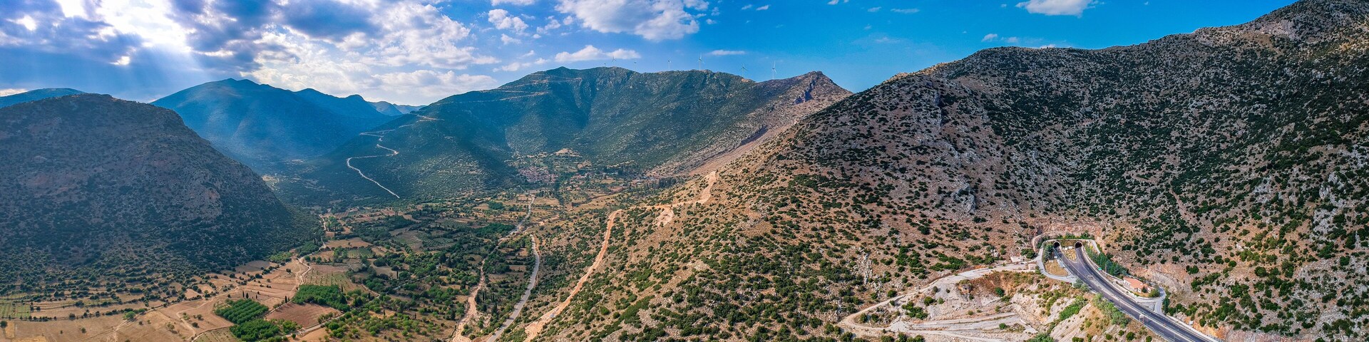 A mountainous landscape with winding roads, green fields, and wind turbines.