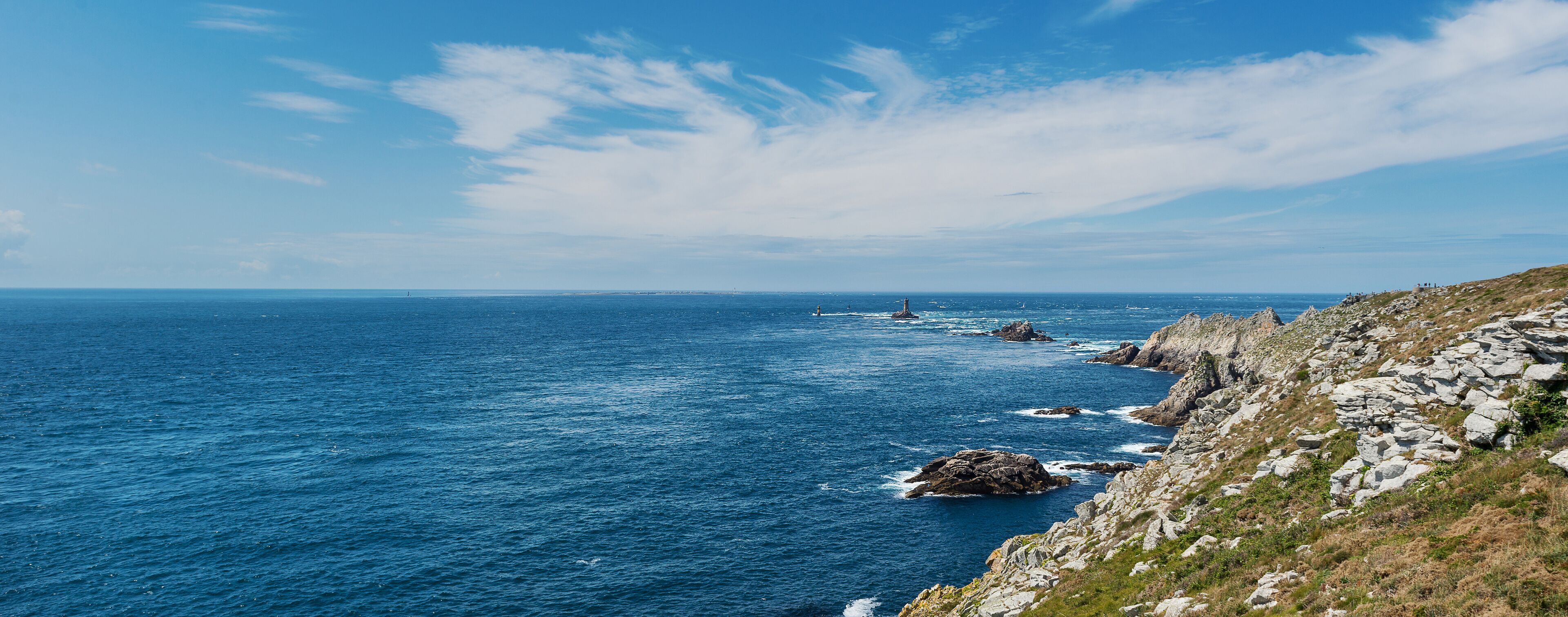 A coastal landscape with rocky cliffs, a lighthouse, and the ocean.