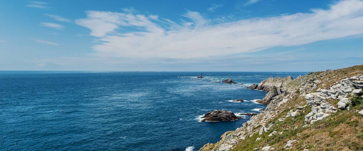 A coastal landscape with rocky cliffs, a lighthouse, and the ocean.
