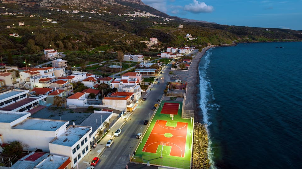 A coastal town with a beach, a road, and a basketball court.
