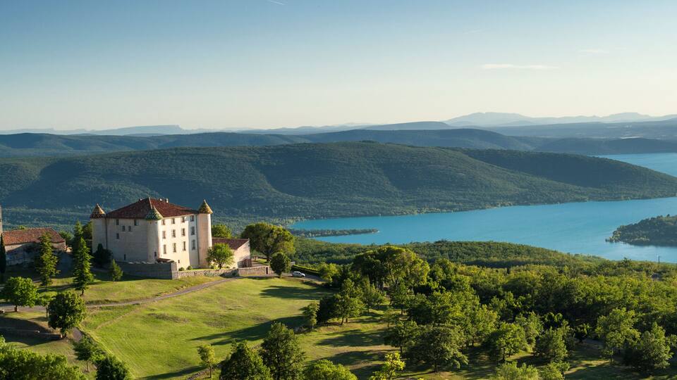 A castle surrounded by lush greenery and a lake.