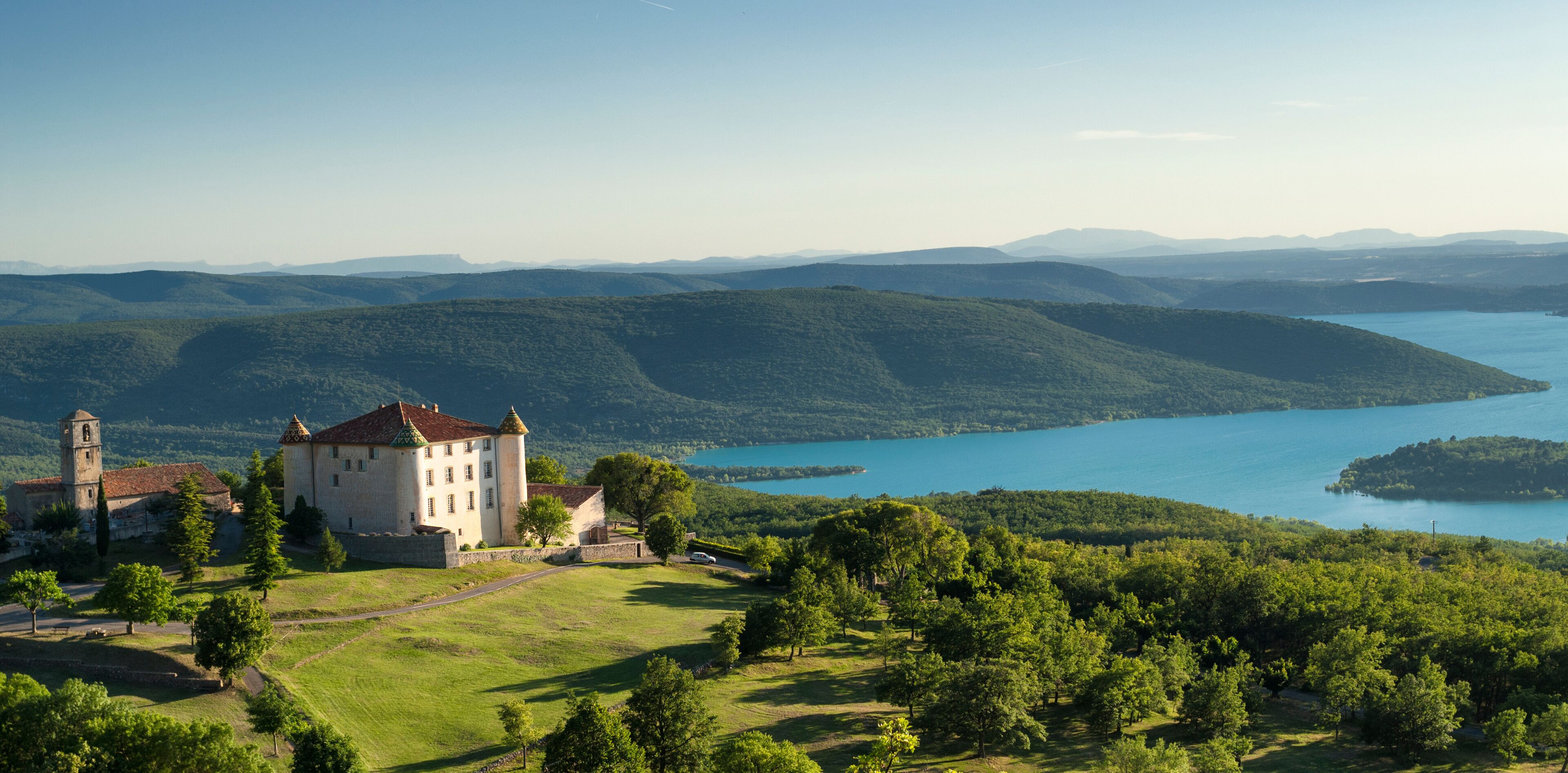 A castle surrounded by lush greenery and a lake.