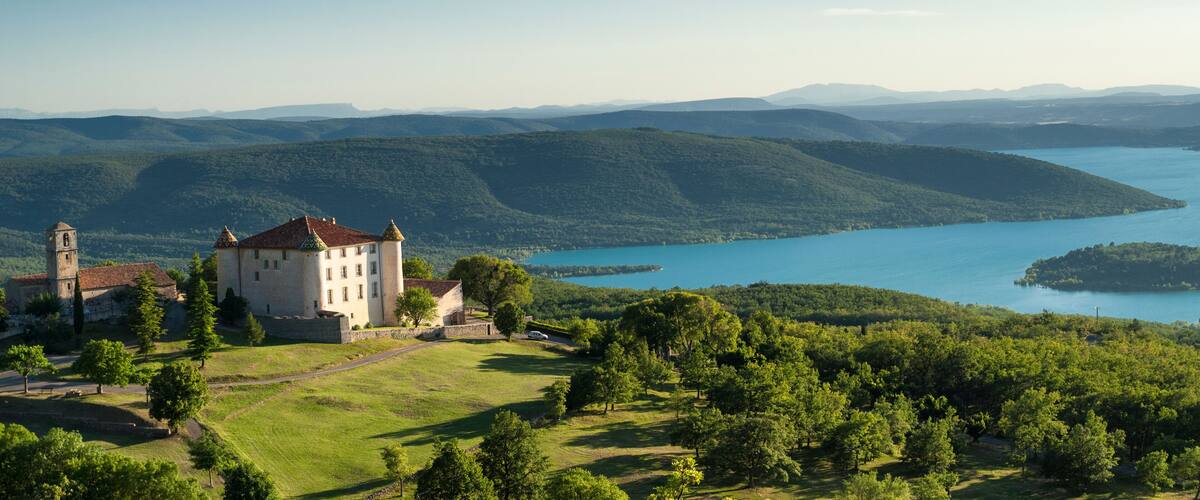 A castle surrounded by lush greenery and a lake.