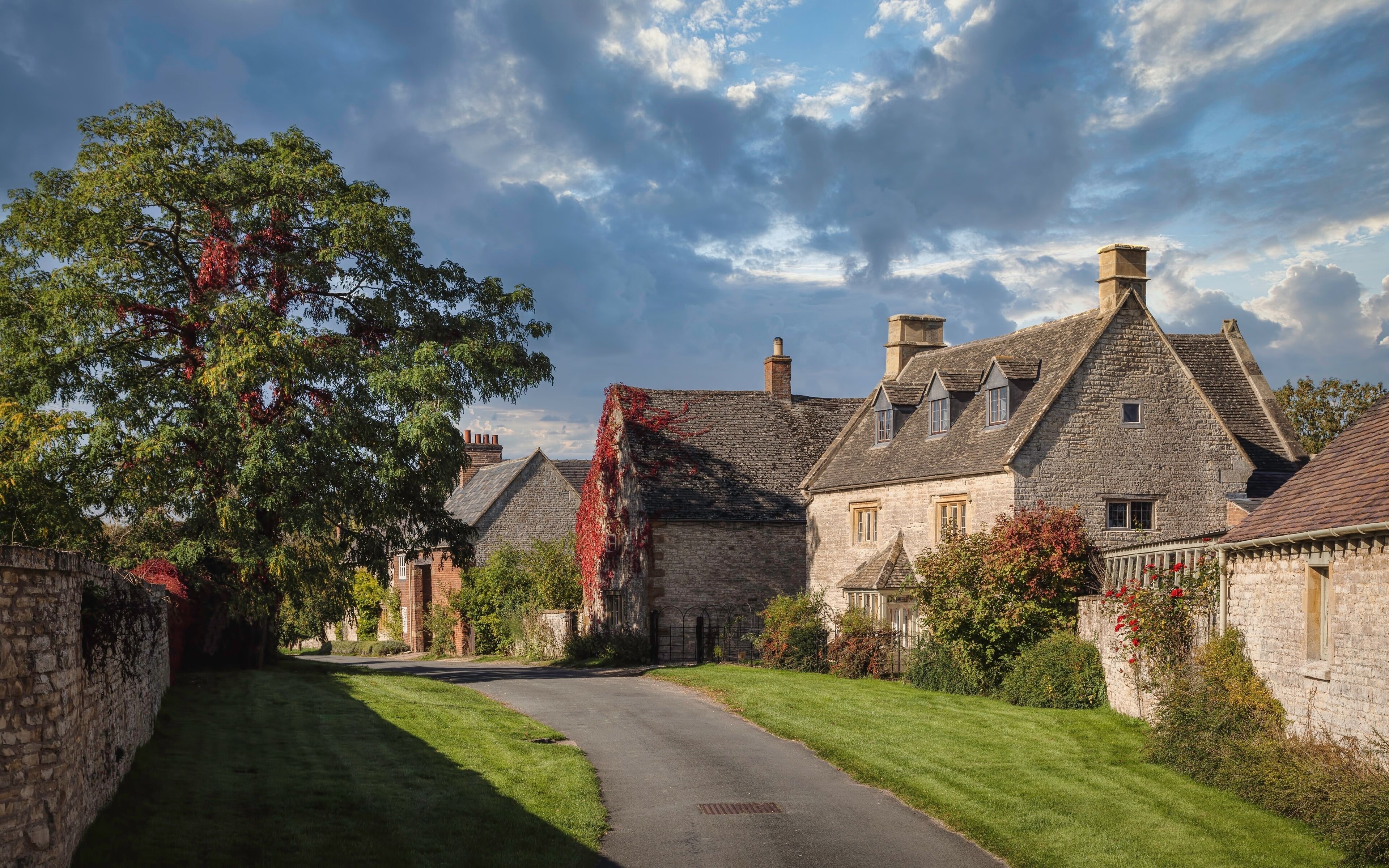 A stone house with a thatched roof, surrounded by lush greenery and a clear sky.