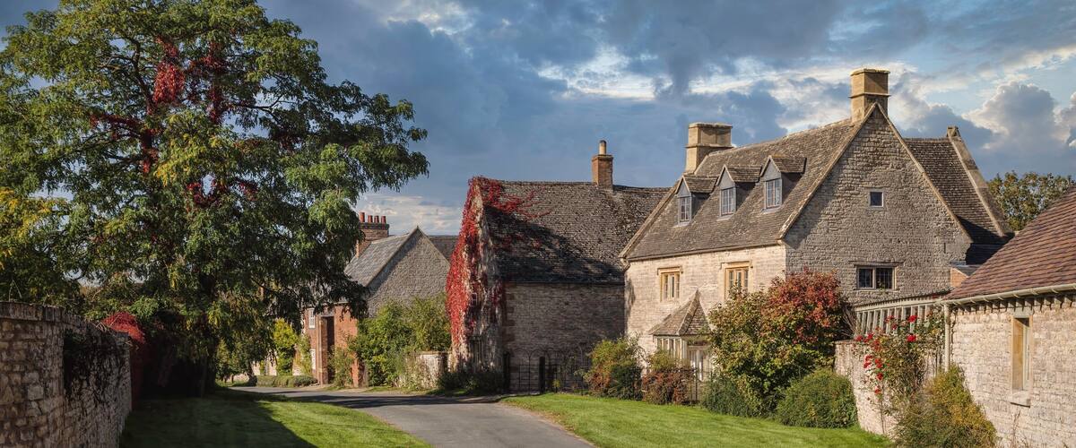 A stone house with a thatched roof, surrounded by lush greenery and a clear sky.