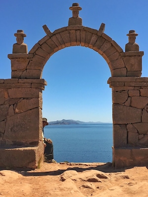 An ancient stone archway overlooking a calm sea with distant mountains.