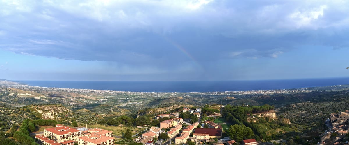 A coastal town with red-roofed buildings, a clear sky, and a distant view of the sea.