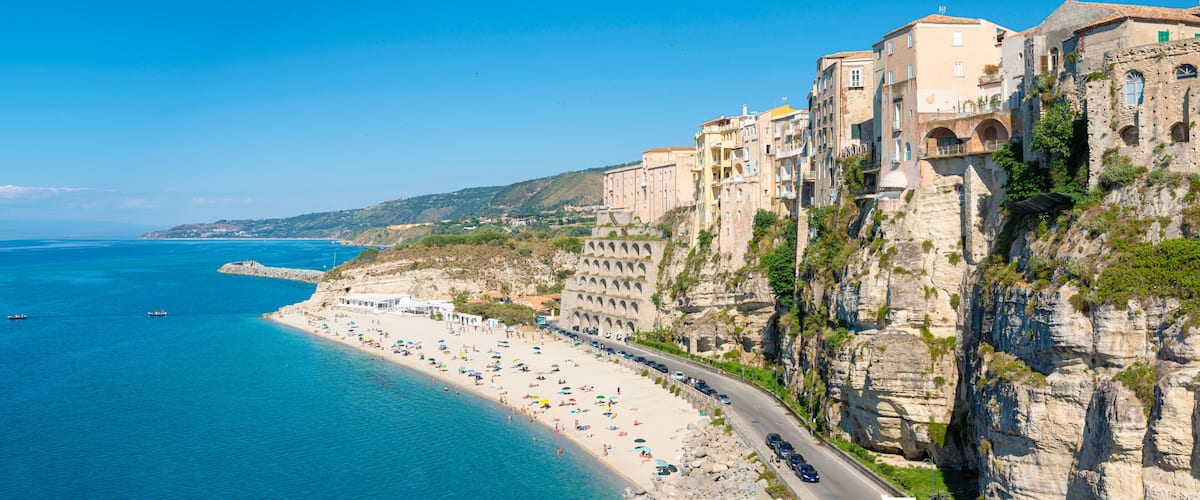 A coastal town with a beach, a cliffside road, and historic buildings.