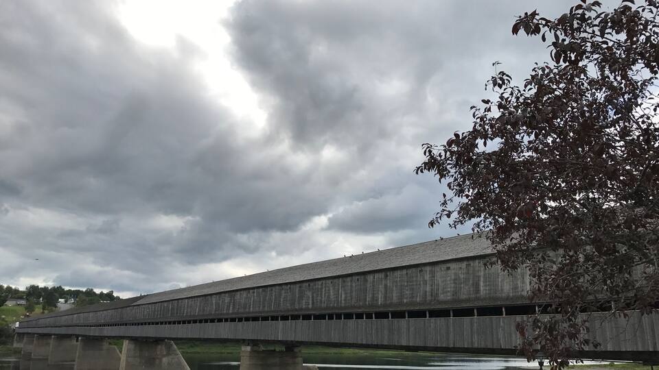 A large concrete bridge over a calm river with people walking on the riverbank.