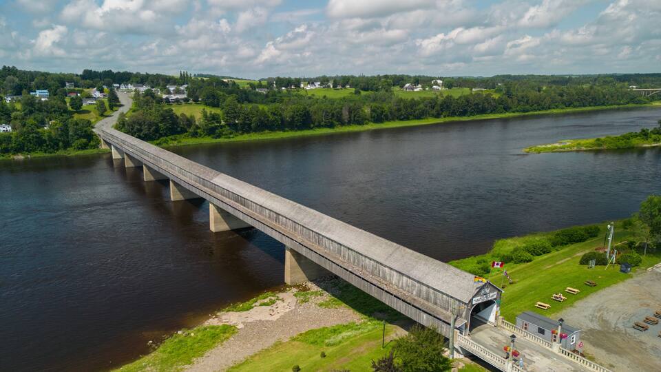 A long bridge over a river with a small town and green fields in the background.
