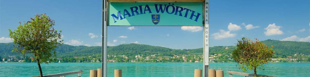 A wooden pier with a sign reading "Maria Worth" and a view of a lake with houses in the background.