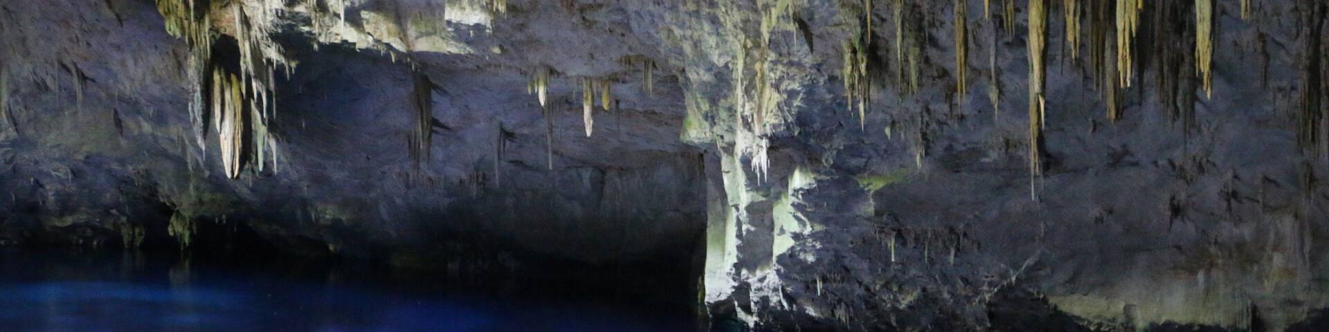 A cave with stalactites hanging from the ceiling and a pool of water at the bottom.
