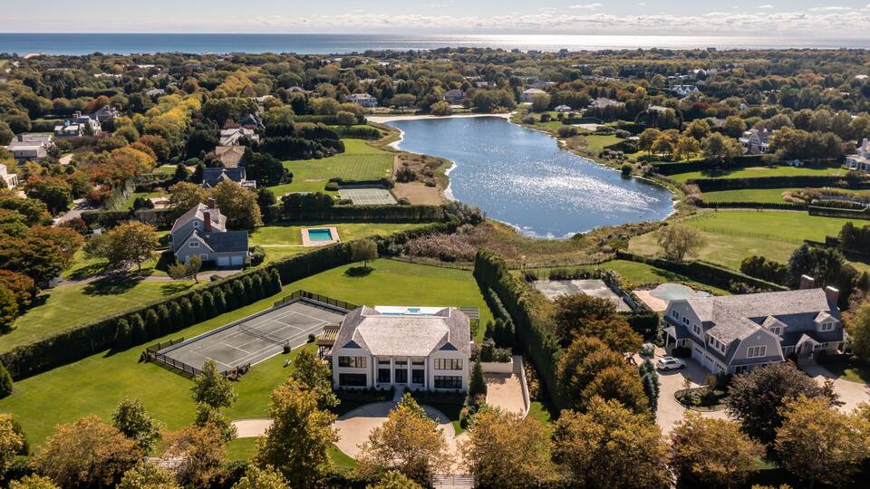 A lake surrounded by residential properties, a tennis court, and a large house with a swimming pool.