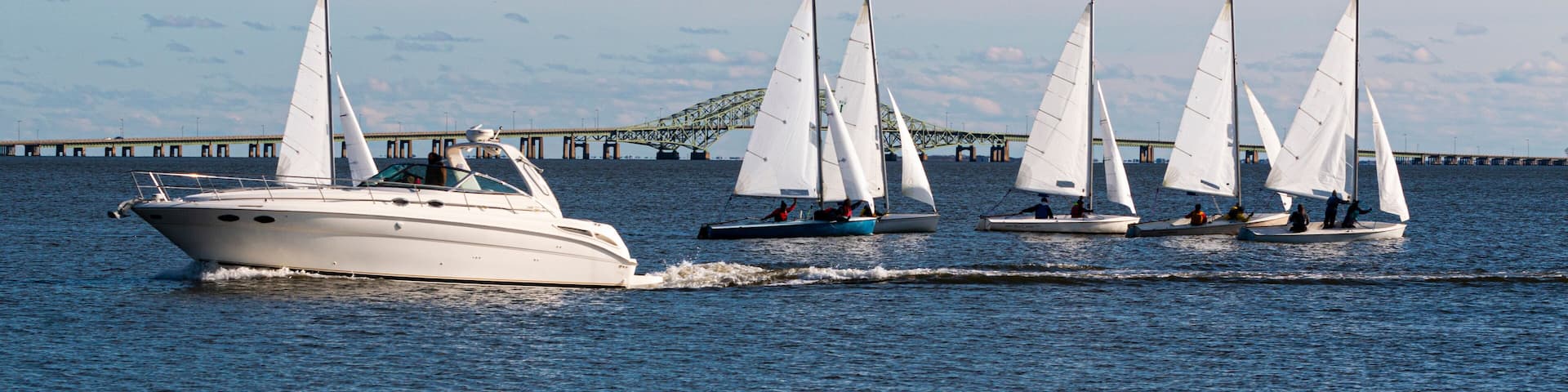 Two person sailboats in December regatta with large motorboat passing infront of them and bridge in background