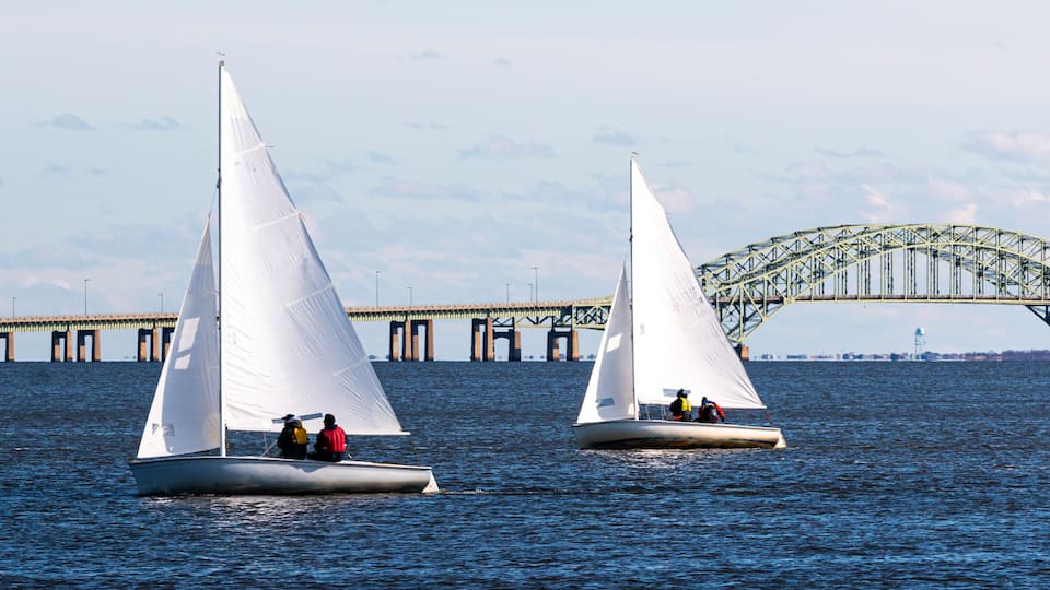 Two sailboats on a body of water with a large bridge in the background.