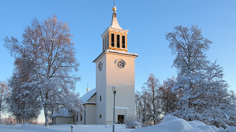A church with a clock tower, surrounded by snow-covered trees.