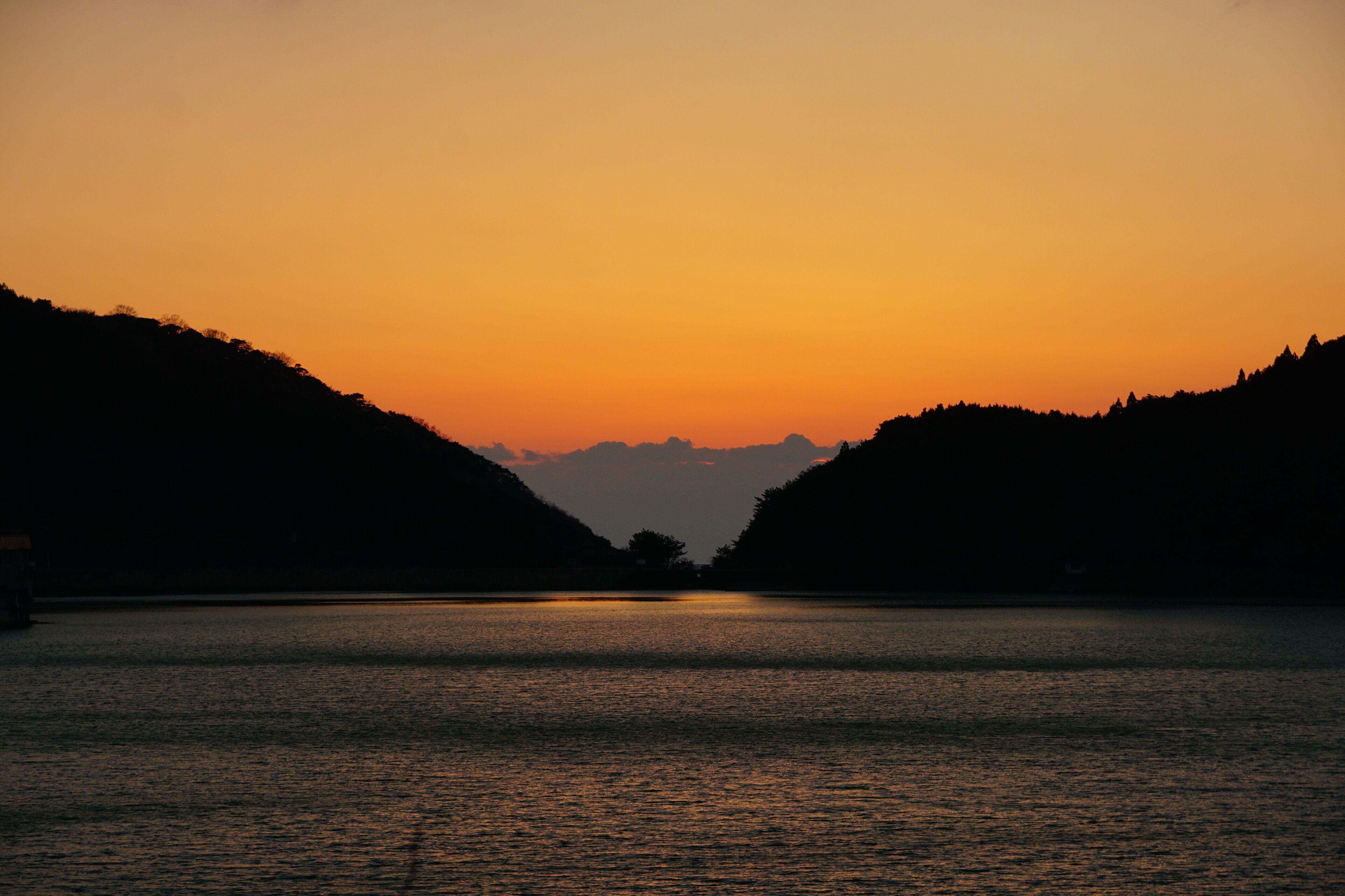 Um pôr do sol sobre um rio calmo, com colinas em ambas as margens.