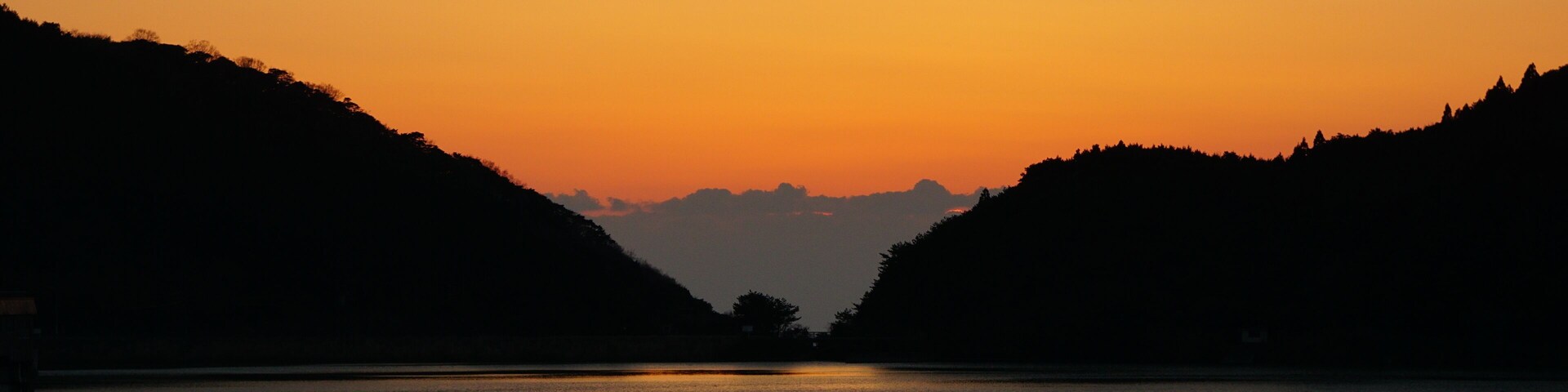 Um pôr do sol sobre um rio calmo, com colinas em ambas as margens.