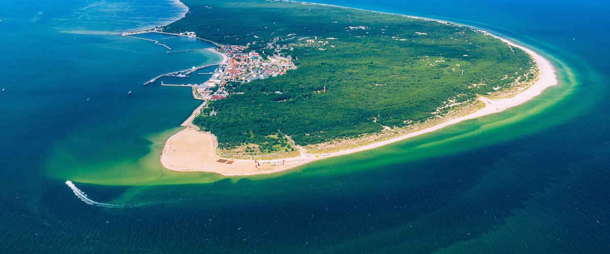 An aerial view of a coastal island with a beach, a small town, and a clear blue sky.
