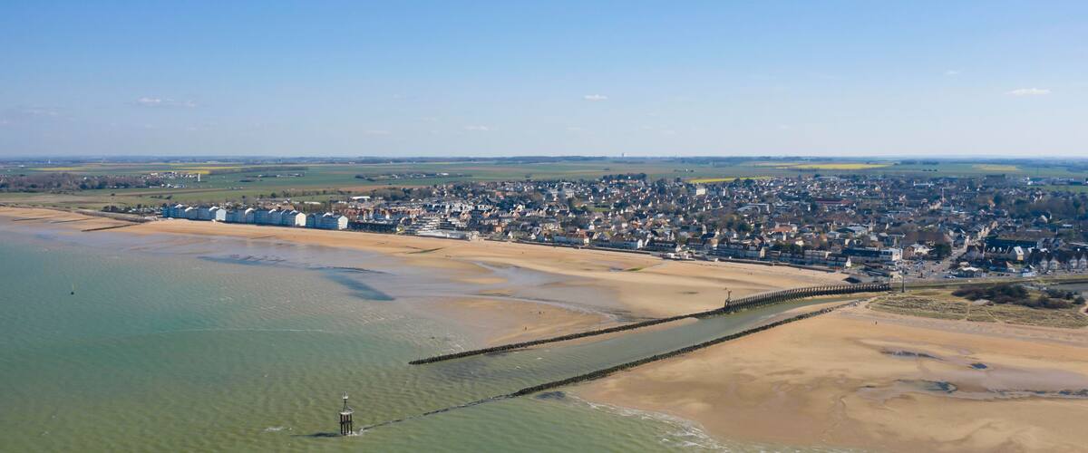 An aerial view of a coastal town with a sandy beach, a pier, and a clear blue sky.