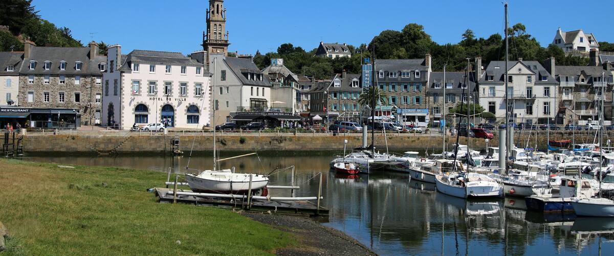 A marina with boats docked, a prominent church with a tower, and a hotel named 'Hotel de Ville' in a coastal town.