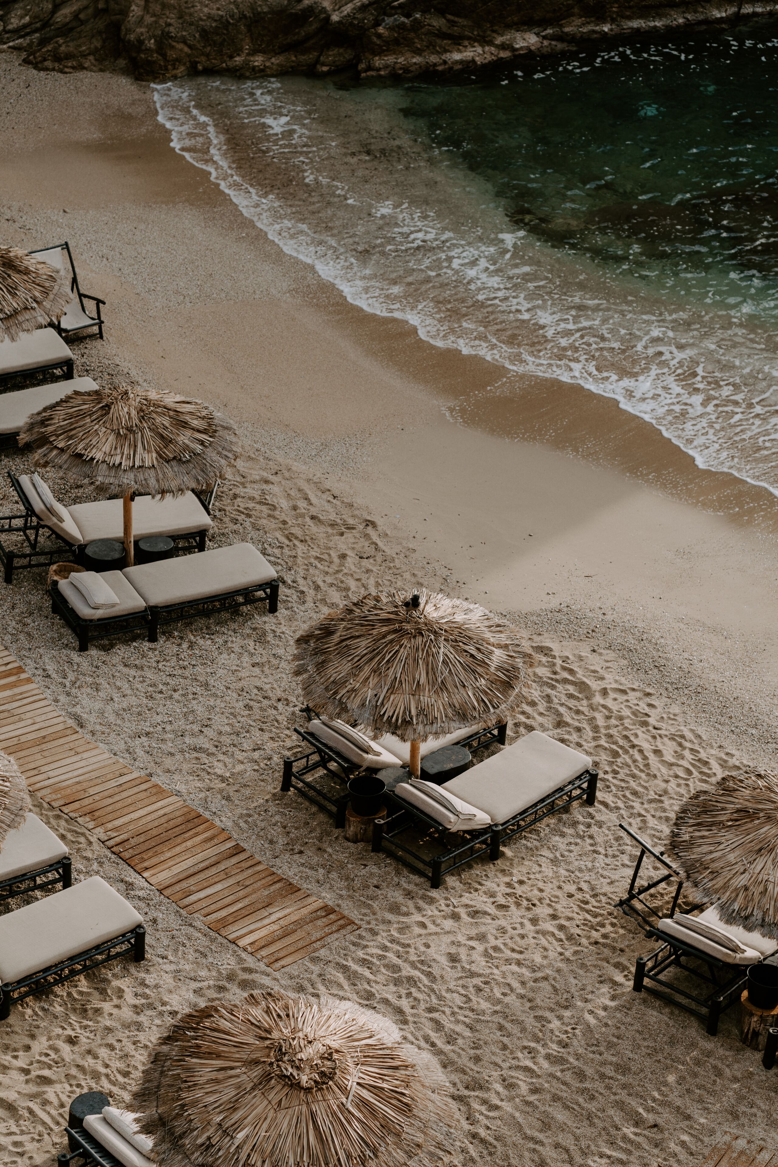 Relaxing scene at a holiday lounge deck by the sea overlooking blue waves and ocean, sun reflecting in water, blue sky and rocks in the background